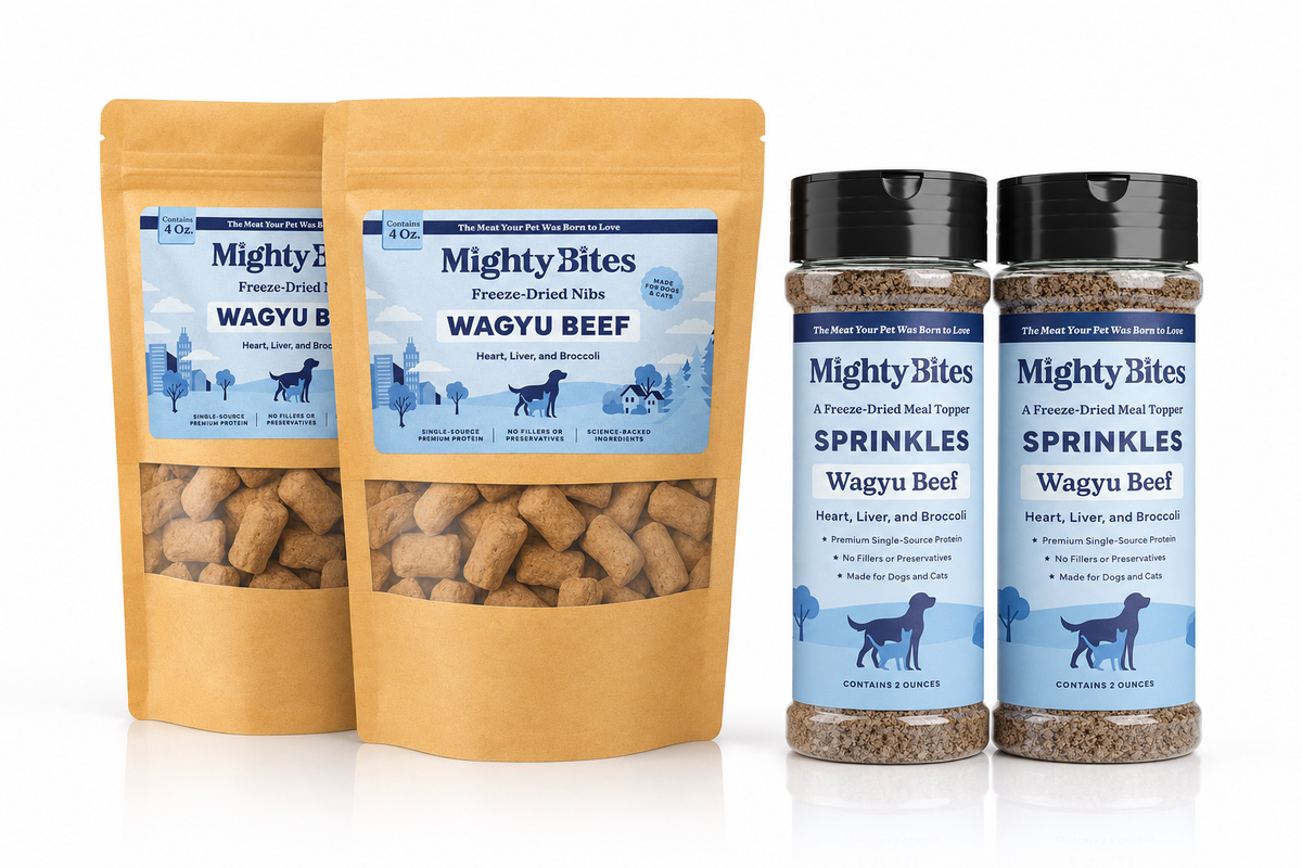 Two stand-up pouches and two clear plastic jars of Mighty Bites dog and cat treats and sprinkles on a white background. The treats are Wagyu Beef with heart, liver and broccoli freeze-dried nibs in two tan pouches and sprinkles in two clear jars, all with blue and white labels.