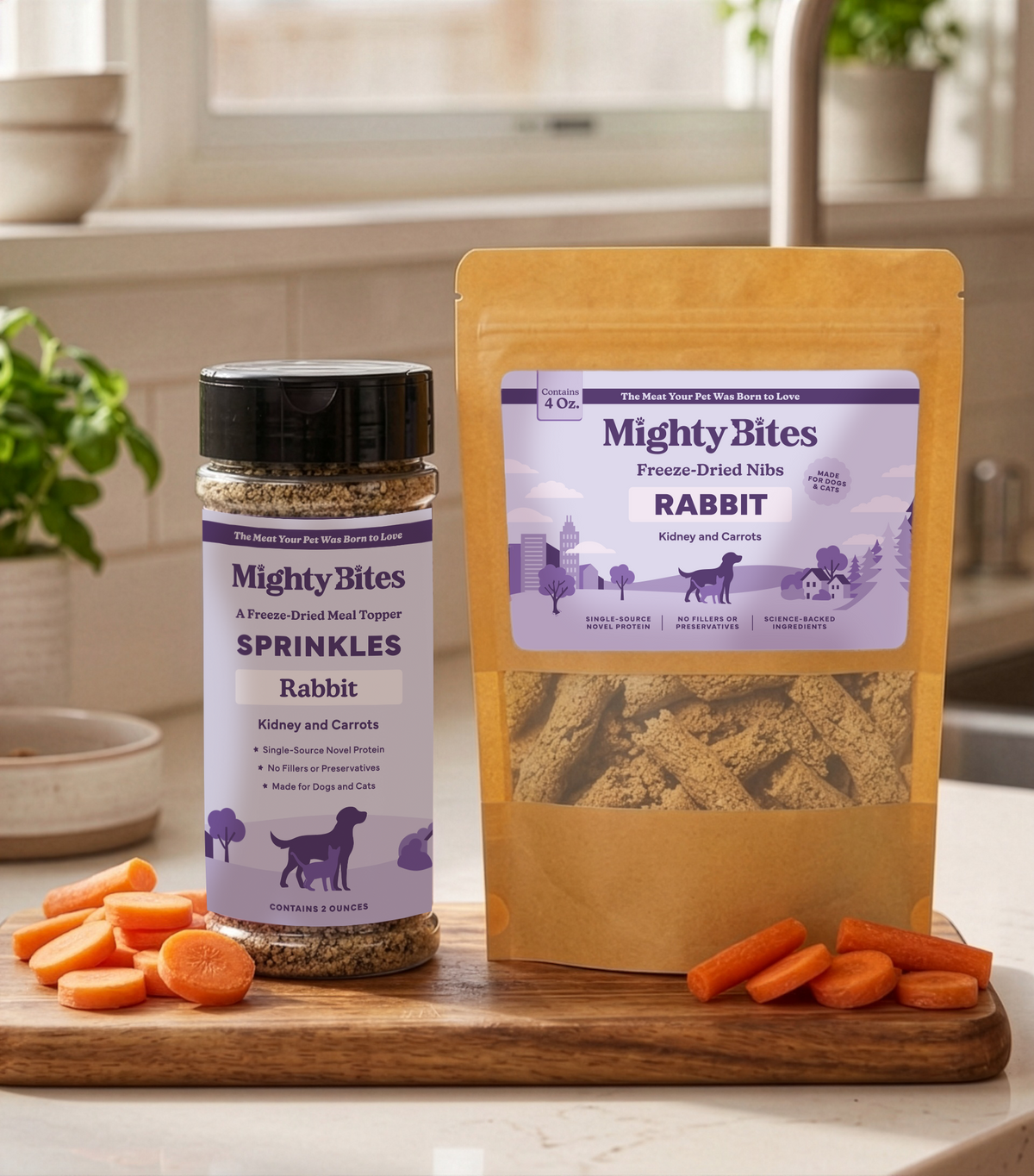 A jar of Mighty Bites Rabbit, kidney and carrot Sprinkles and a stand-up pouch of Mighty Bites Freeze-Dried Nibs also in rabbit are displayed on a wooden cutting board with carrot slices in a bright kitchen setting. A dog or cat treat and meal topper. 